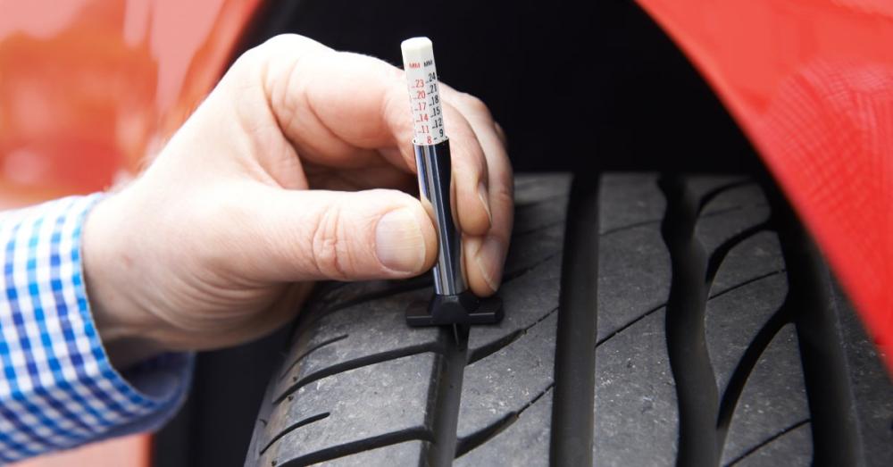 A person's hand holds a tire depth gauge against a tire to see how much tread it has left. There appears to be a lot left.