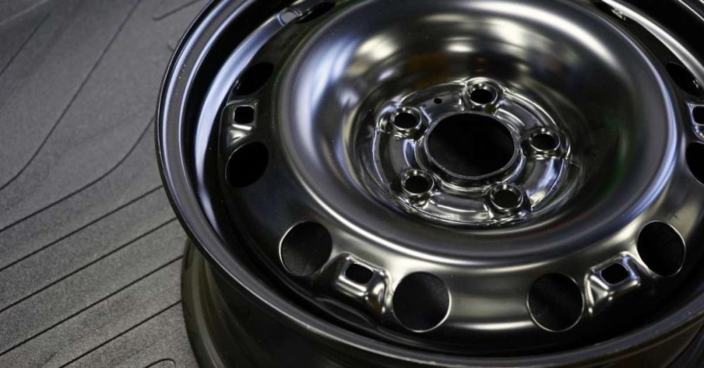 A close up of a black car rim lying down on its side. The wheel is sitting on top of a black rubber mat.