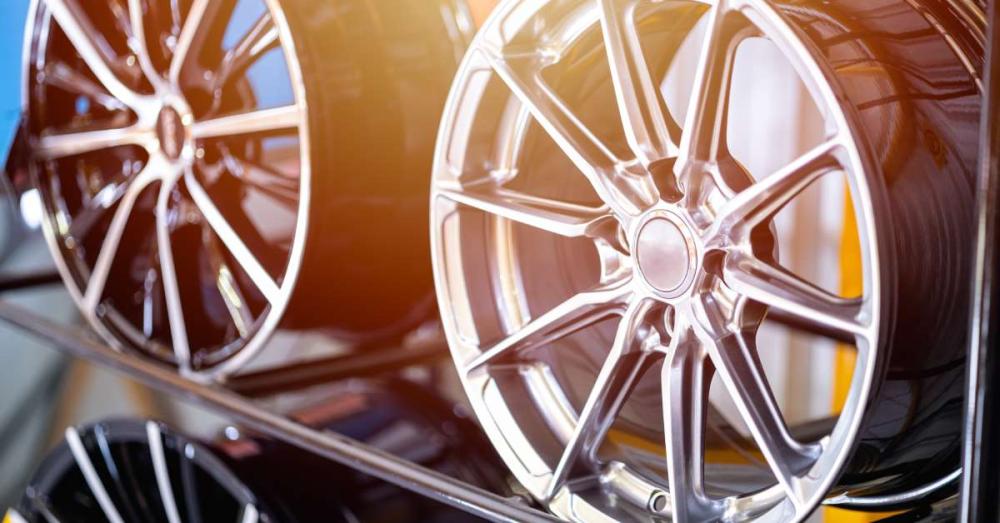 Two car rims sitting side-by-side on a shelf together. You can also see a third rim sitting on the shelf below them.