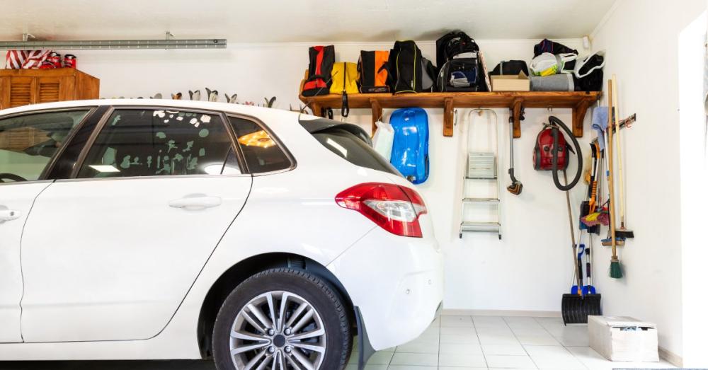 The back end of a small white SUV parked in a garage. There are a lot of tools and bags on the wall behind the car.