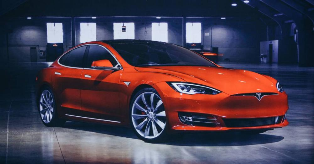 A red Tesla Model S sitting in the middle of an empty showroom floor. There are some windows in the background.