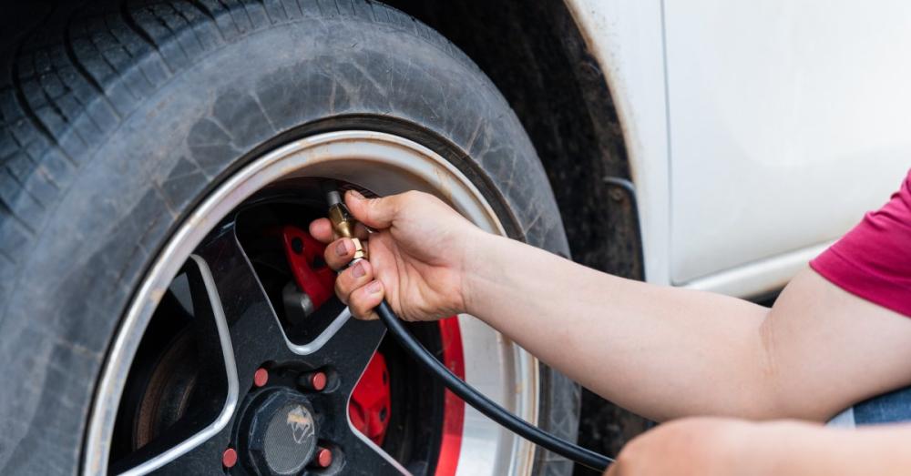 A man using an air hose to fill up his car's tire. He holds the hose to the tire's valve stem to connect it.