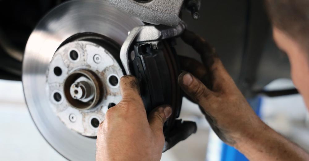 A man working on the brake system of a car. He has the brake mount open and is inspecting the pads.