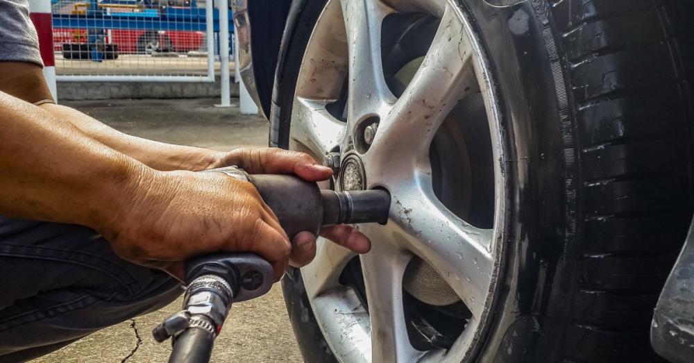 A mechanic using a pneumatic wrench to remove the lug nuts off a wheel before taking the wheel off the base.