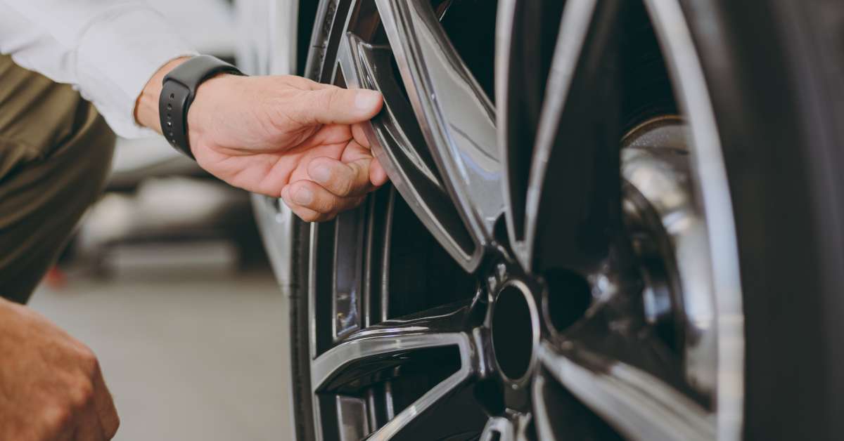 A man reaches out and touches the spokes of a wheel. The wheel is very clean and attached to a white car.