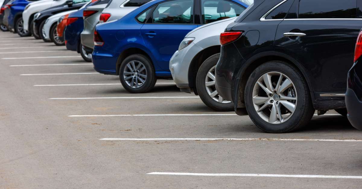 A row of cars is parked side-by-side in a parking lot, and the wheels of the vehicles are in focus.