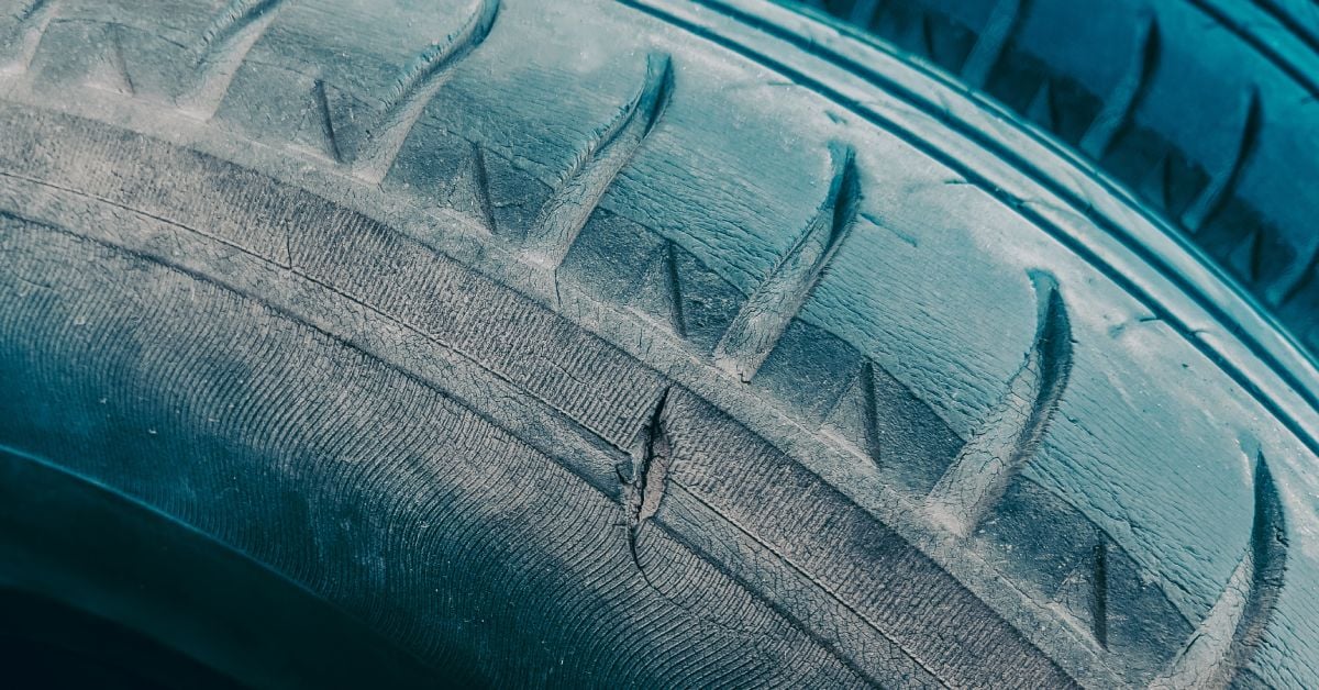 A close up view of an old tire. The tread has worn away considerably and there is a noticeable tear.